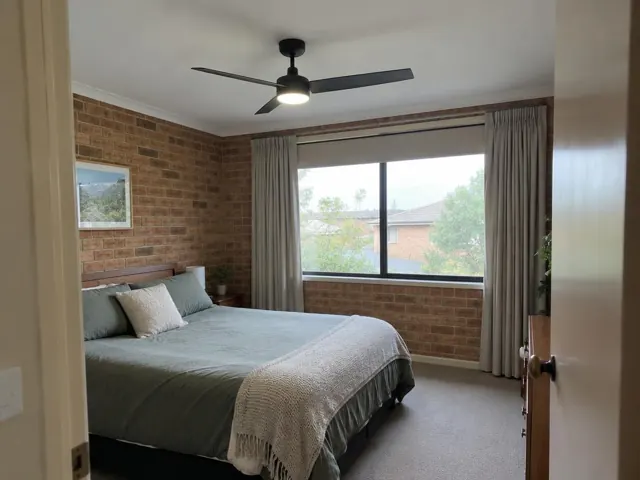 Ceiling fan in a brick-walled bedroom with a window and bed in Ashtonfield